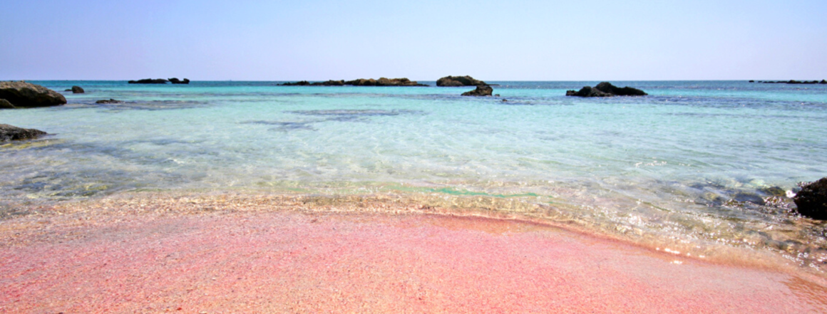 Pinker Strand Elafonissi, Griechenland - Türkisblaues Wasser mit pinken Sand und kleinen Felsen im Wasser
