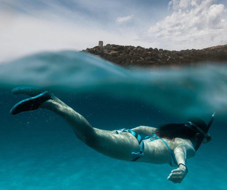 Frau in einem blau schwarzem Bikini, die beim Schnorcheln im blauen Wasser abtaucht 