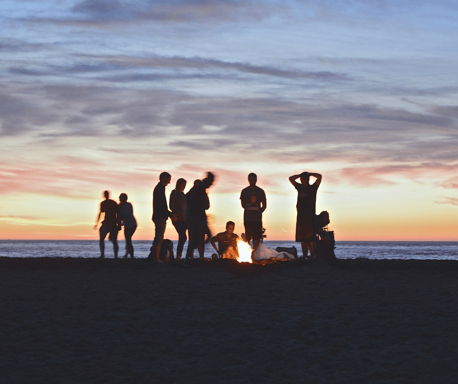 Eine Gruppe, die am Strand ein Lagerfeuer macht, während die Sonne untergeht