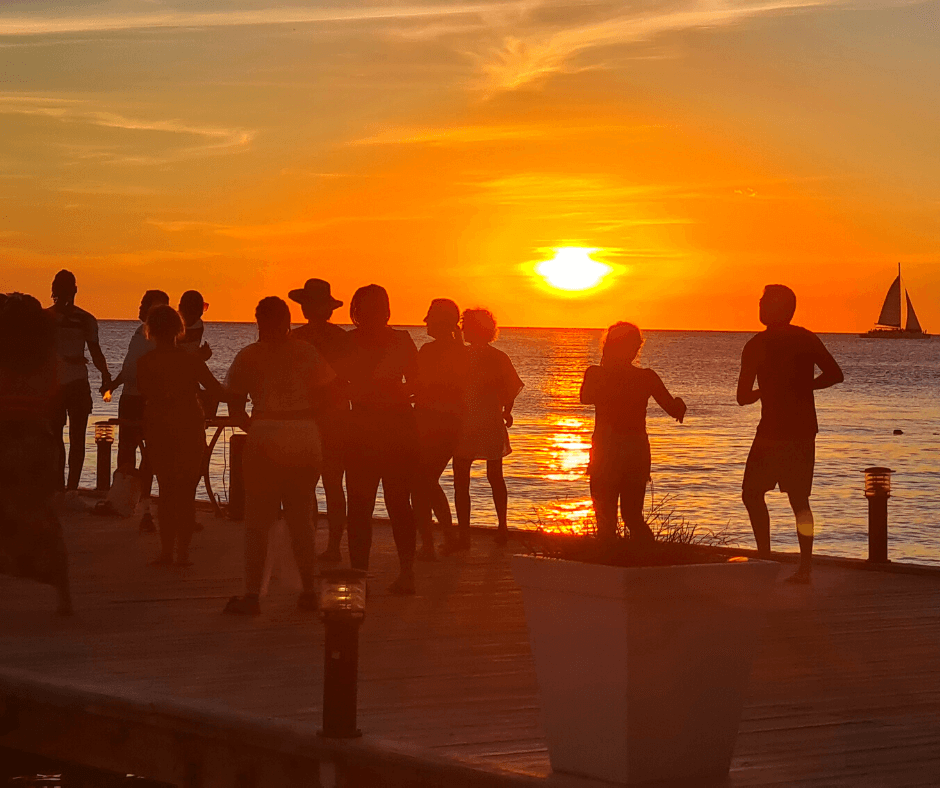 Verschiedene Personen, die an einer Promenade bei Sonnenuntergang spazieren oder joggen, mit einem Segelboot am Horizont