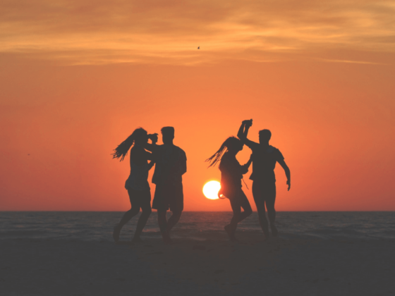 Vier Personen, die am Strand bei Sonnenuntergang tanzen mit orange rotem Himmel