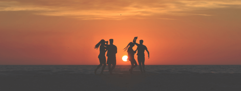 Vier Personen, die am Strand bei Sonnenuntergang tanzen mit orange rotem Himmel