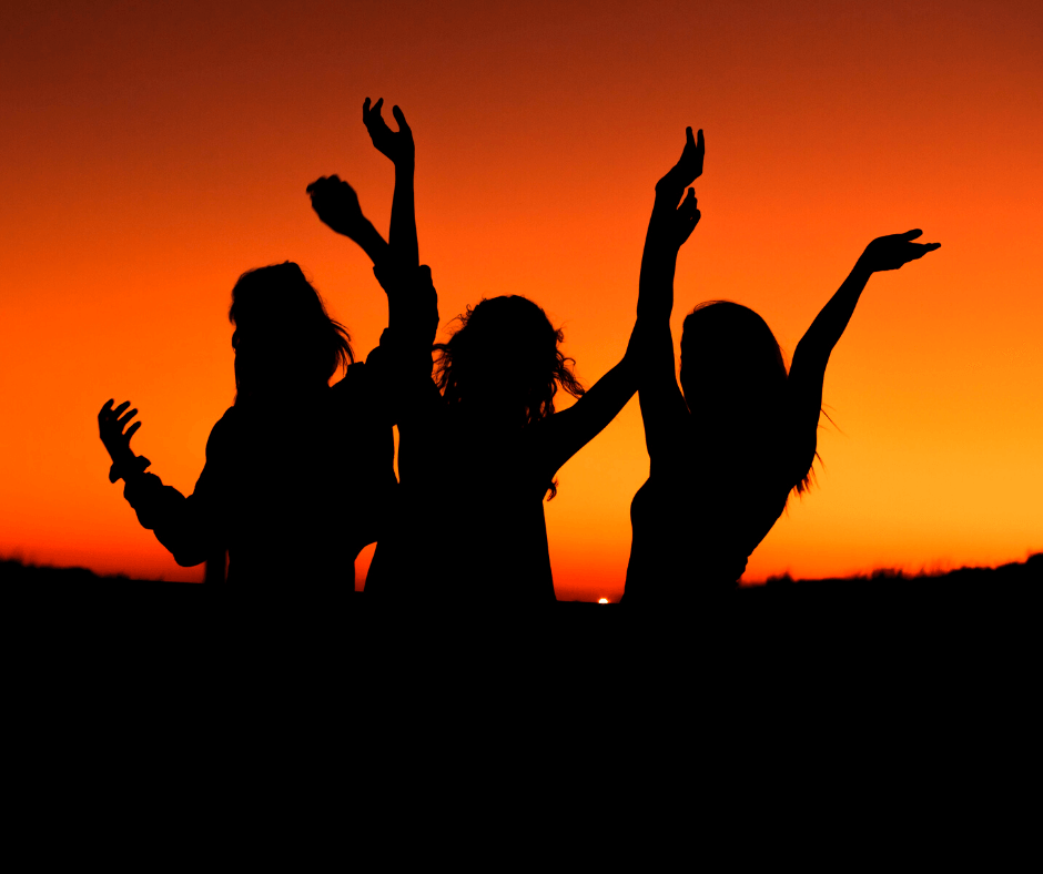 Drei Personen, die bei Sonnenuntergang tanzen, mit orange gefärbtem Himmel 
