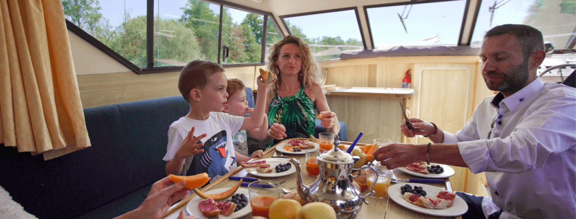 Eine Familie an Bord eines Bootes bei einem reichhaltigen Frühstück mit Tee, Saft und Früchten