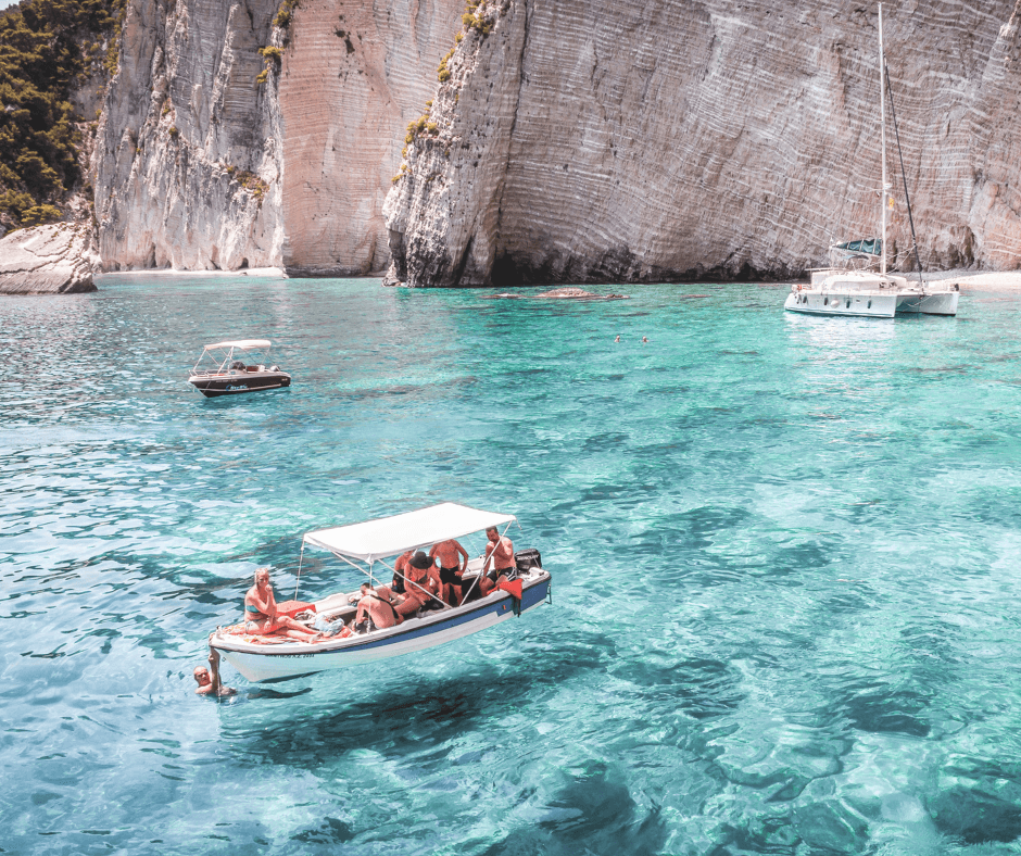 Boot mieten für einen Tag, Motorboote und Katamaran auf dem türkisfarbenen Wasser neben einer Felsenklippe, Personen auf dem Motorboot, schwimmende Personen im Wasser