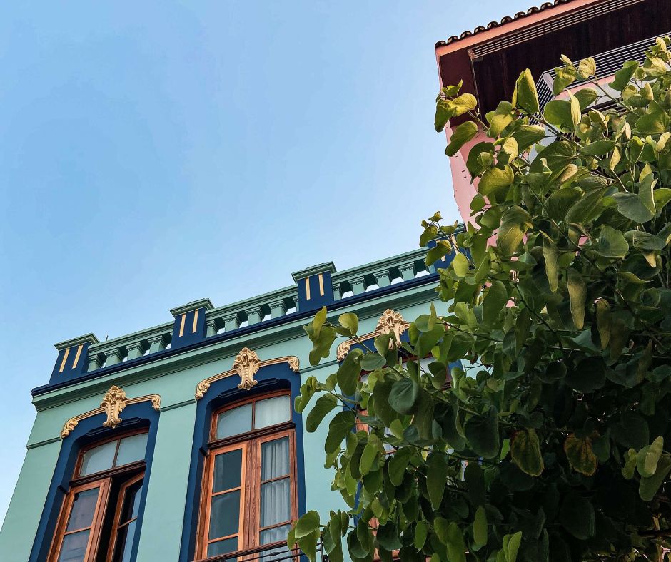 Hausfassade in verschiedenen Blautönen mit goldenen Verzierungen. Rechts im Vordergrund sieht man einen Zitrusbaum.
