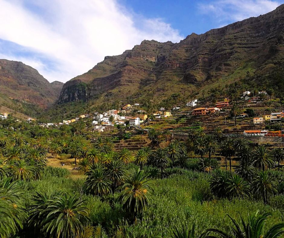 Großes begrüntes Tal mit kleinen bunten Häusern und vielen Palmen. Rechts und links gehen steile Klippen hinauf, die kleine begrünte Terassen haben.