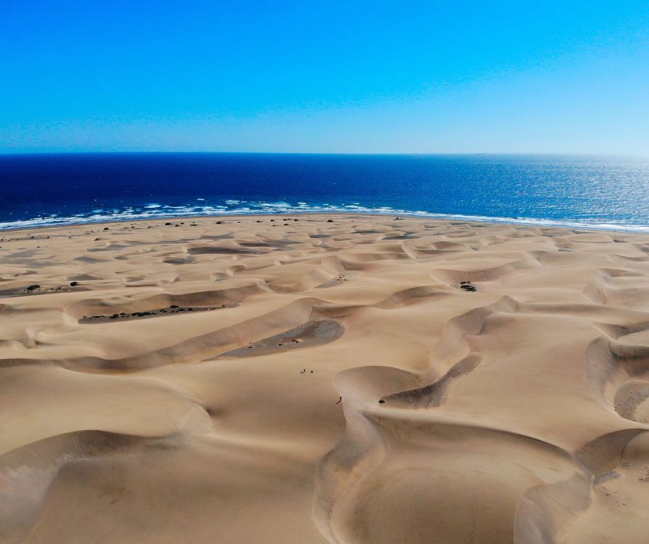 Sanddünen mit tiefblauem Meer im Hintergrund.