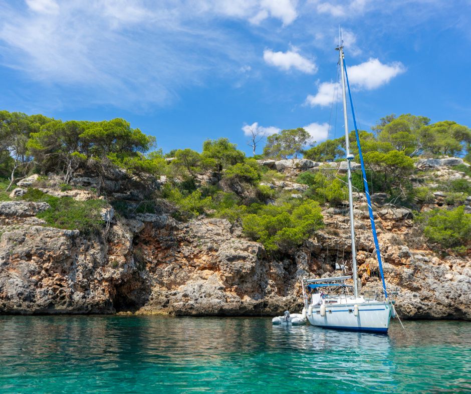 Segelboot in einer Bucht von Mallorca. Man sieht türkises Wasser, braune Felsen und blauen Himmel.