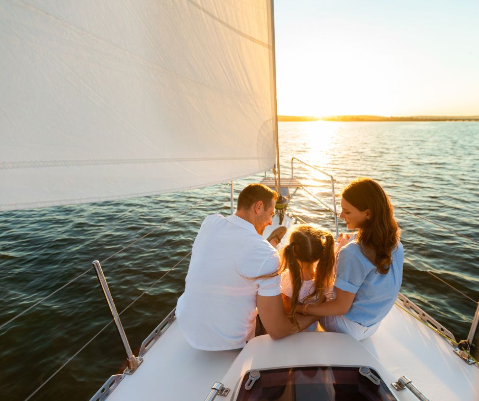 Kleine Familie sitzt an Bord eines Segelbootes und schaut in den Sonnenuntergang.