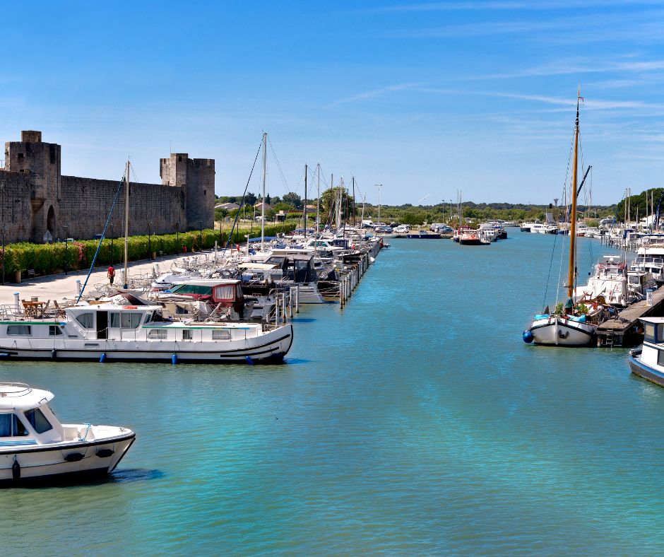 Ein Hausboot günstig mieten in einem Hafen. Das Wasser im Hafen ist blau und am linken Rand sieht man eine Burg mit Büschen davor.