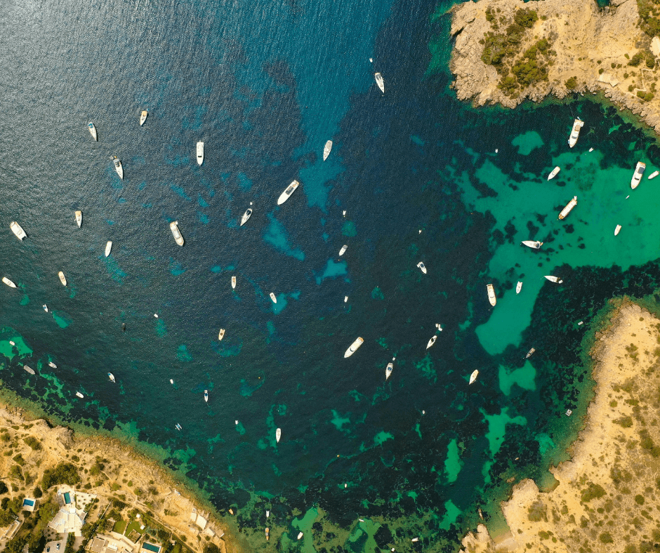 Viele Boote in einer Bucht auf Ibiza. Die Aufnahme ist von oben gemacht und zeigt das blaue Wasser.