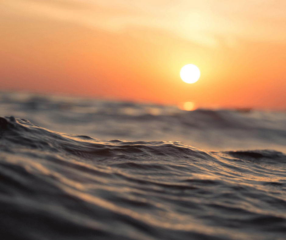 Man sieht Wellen im Vordergrund und im Hintergrund einen orangefarbenen Sonnenuntergang, den Sie während Ihres Costa Brava Urlaubs genießen können.


