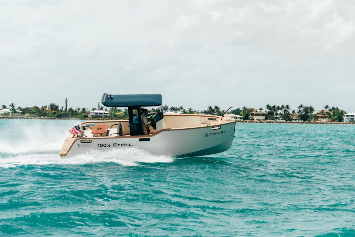 Ein Elektroboot gleitet über türkisfarbenes Wasser, im Hintergrund erheben sich majestätische Palmen. Die Szene strahlt tropische Schönheit und Entspannung aus, während das Boot geräuschlos durch das glitzernde Wasser gleitet.