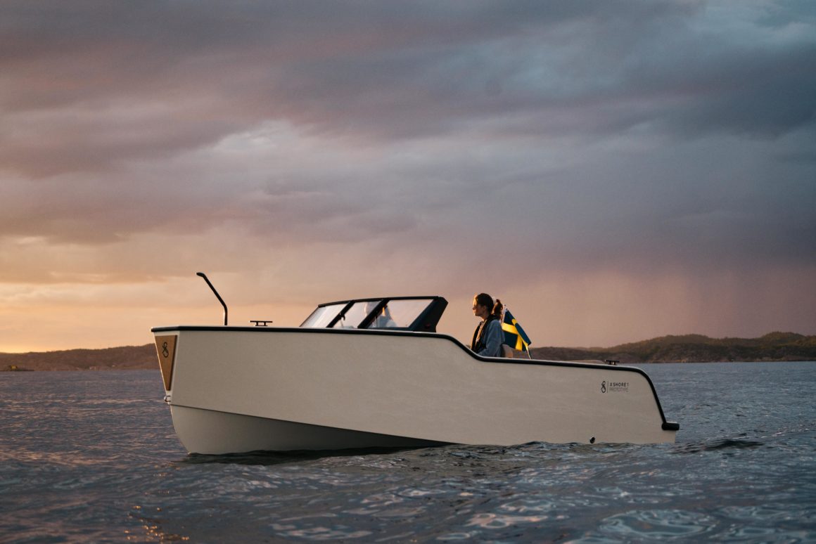 Ein Elektroboot gleitet sanft über das Wasser, eine Frau steht an Bord und genießt die Fahrt. Im Hintergrund ziehen dunkle Wolken auf, begleitet von Regen, während die Sonne langsam untergeht. Die Szene vermittelt Ruhe und Abenteuer zugleich.