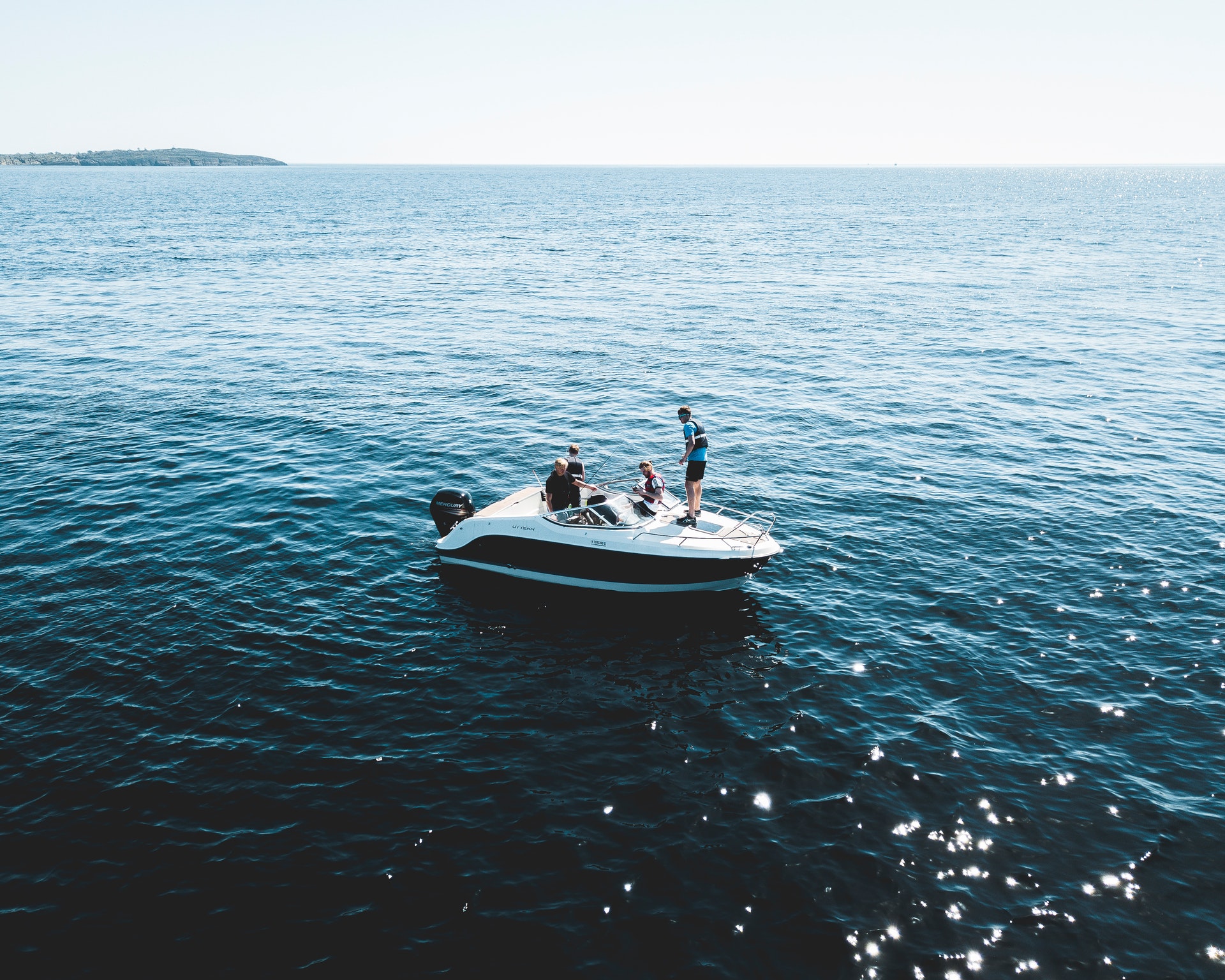 Four people standing on a motorboat in open waters, one small island is visible on the horizon