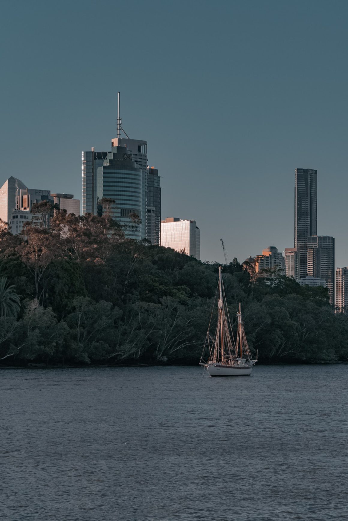 A sailboat sails in front of the city of Brisbane with famous towers of the Brisbane skyline behind it.