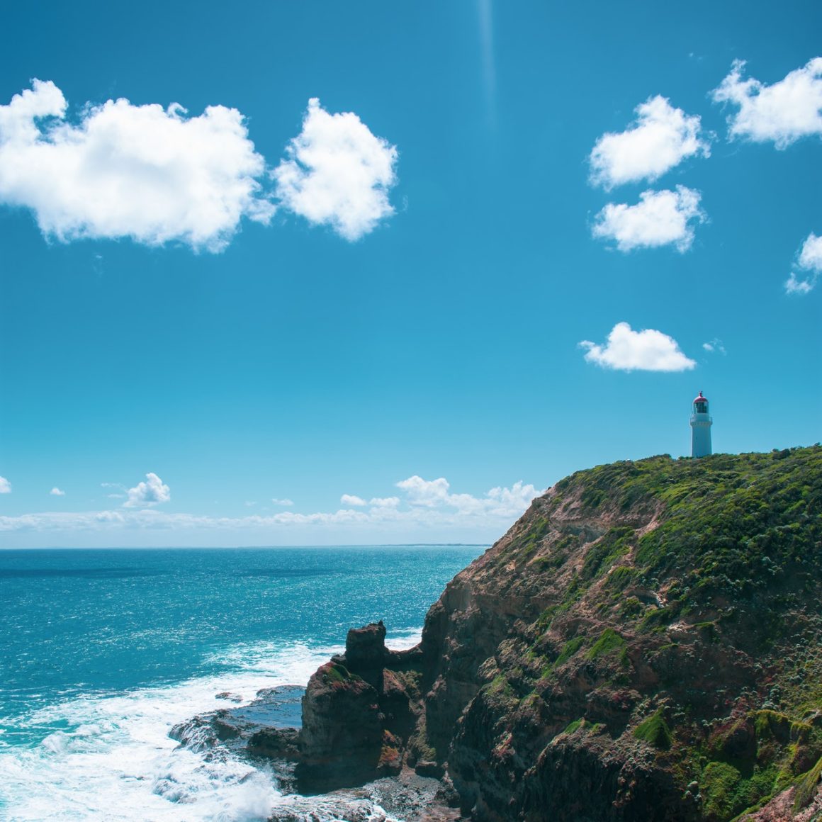 a lighthouse stands on a clifftop overlooking the sea on a clear, sunny day