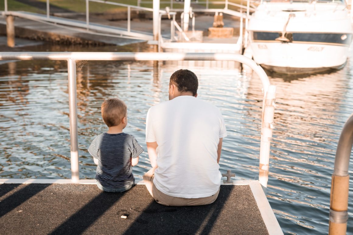 Father and child sitting at the edge of a marina