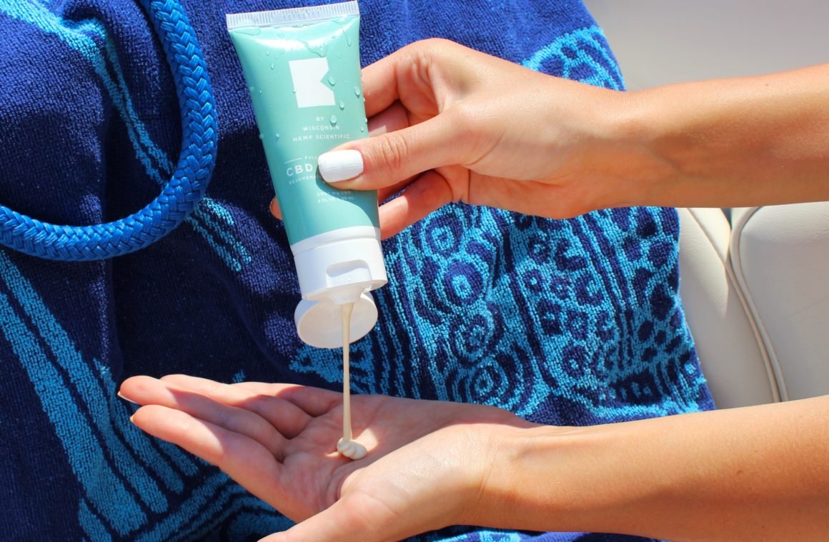 Sunscreen being squeezed out of a light blue tube and onto a hand.