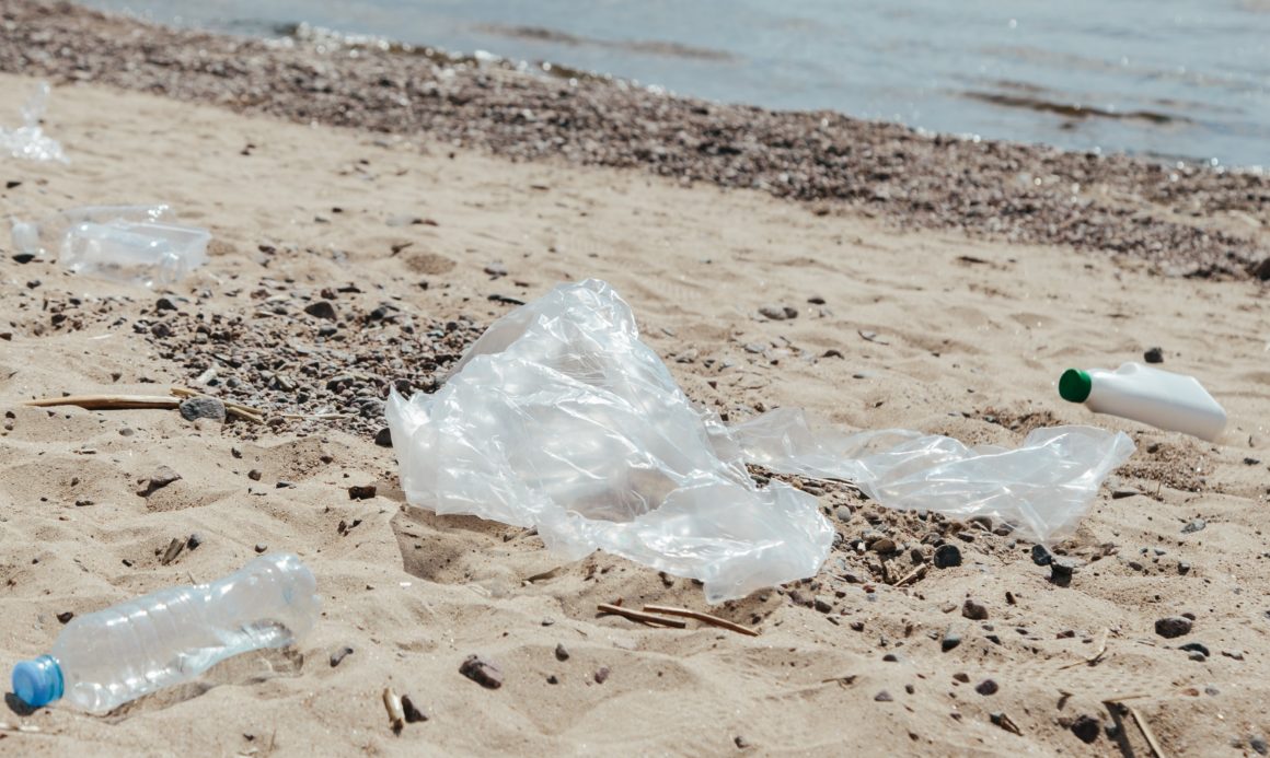 A picture containing plastic garbage on the ground of a sandy beach shore.