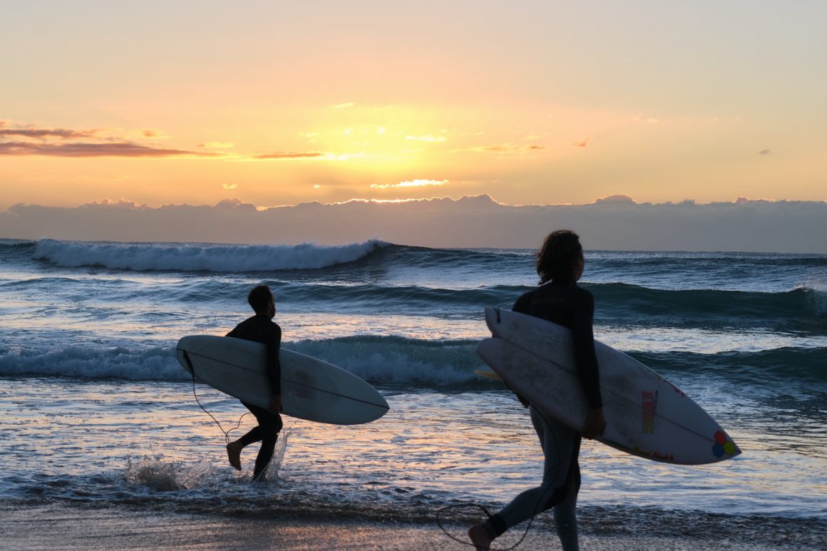 Manly Beach, one of Sydney's best beaches, surfers running into waves at sunset. 