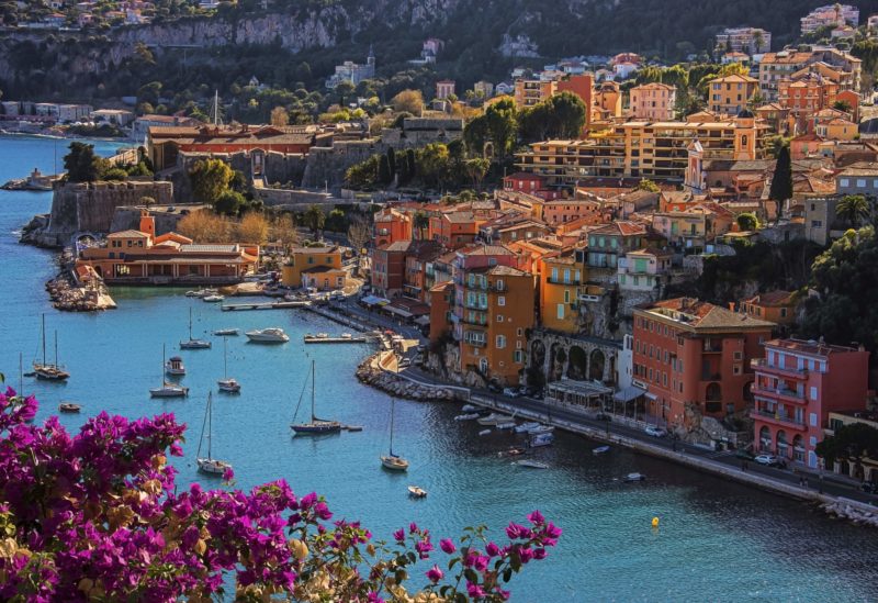 O litoral em Villefranche.  Barcos navegando no mar azul e casinhas coloridas ao fundo