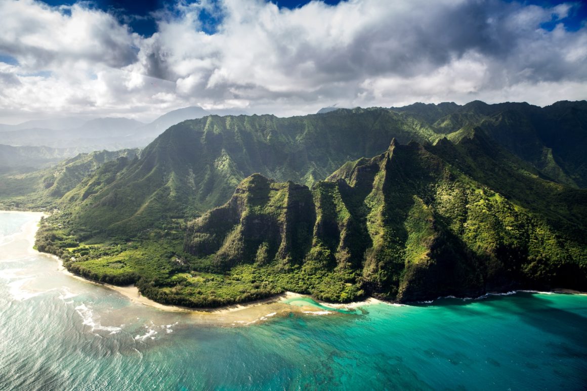 An aerial view of Kauai Island, you can see tall green mountains and turquoise waters.