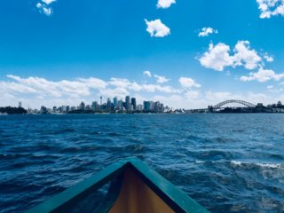 View of Sydney harbour on a sunny day, with skyline in the background and the blue water.