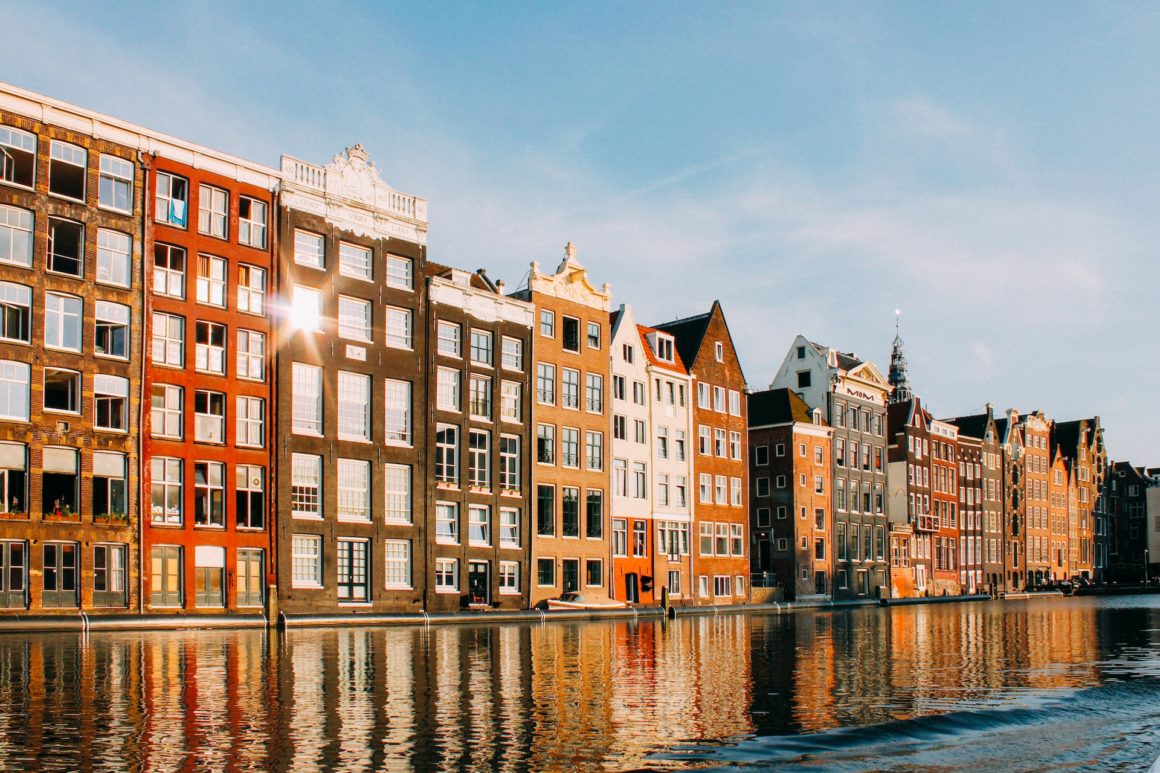 The buildings of Amsterdam that look onto the canal glistening from the sun's light.