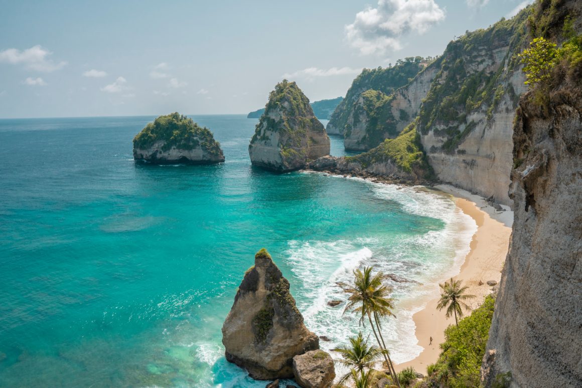 Beach and cliffs in Nusa Penida, turquoise water, waves, palm trees, rock formations