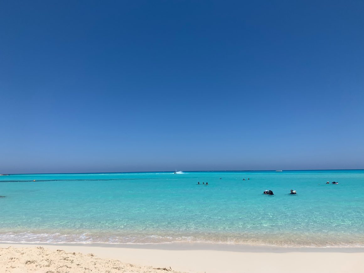 White sand beach, turquoise water, and swimmers under a blue sky.