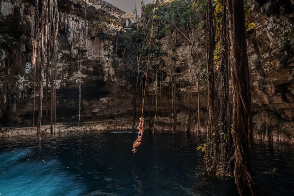 A woman swinging over the blue water in a cenote in Mexico.