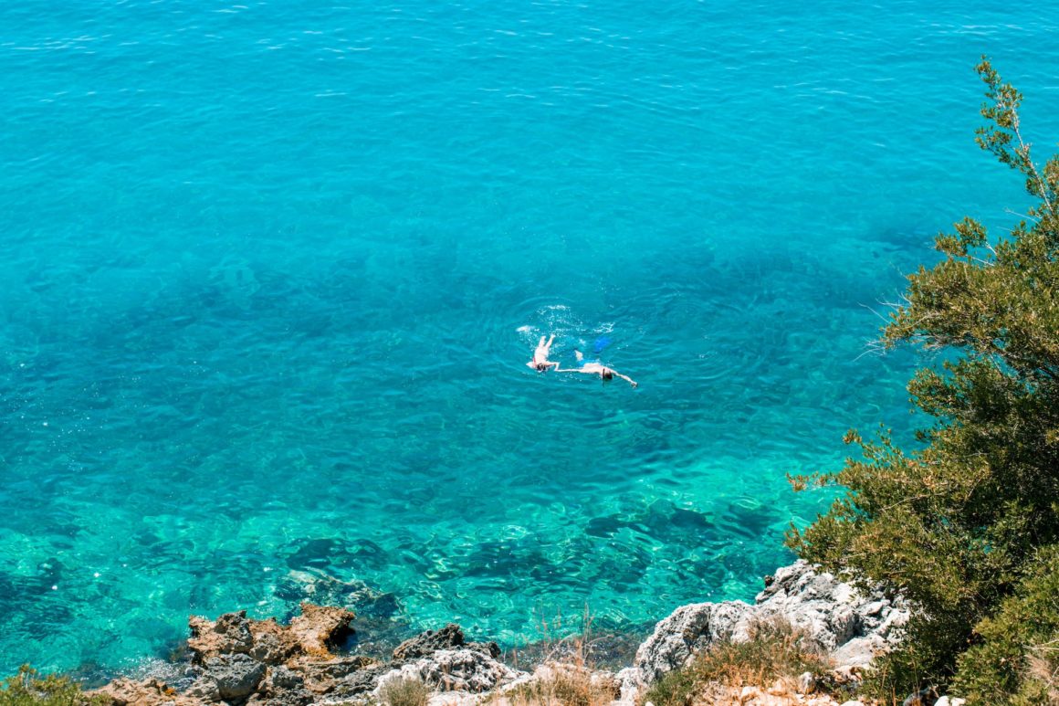 Beach in Albania with crystal-clear waters and tourists snorkelling, one of the best European beaches