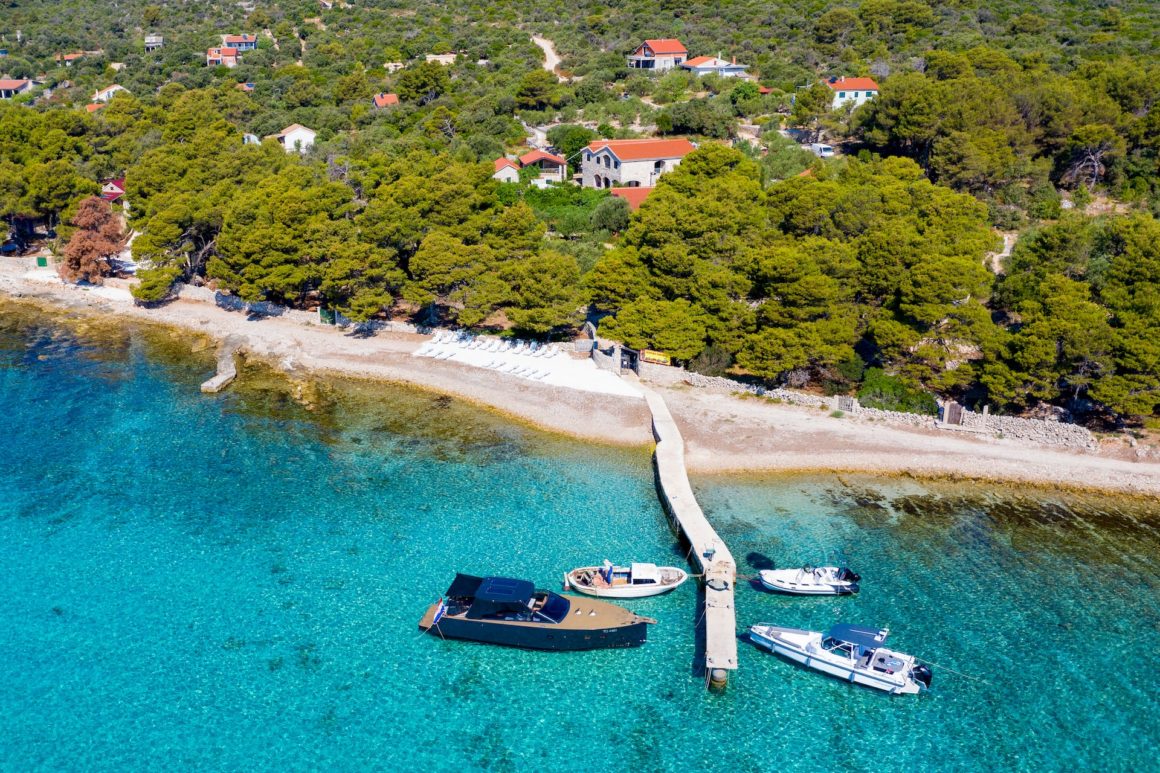 Aerial view of a white sandy beach with jetty, forests and houses in Silba.