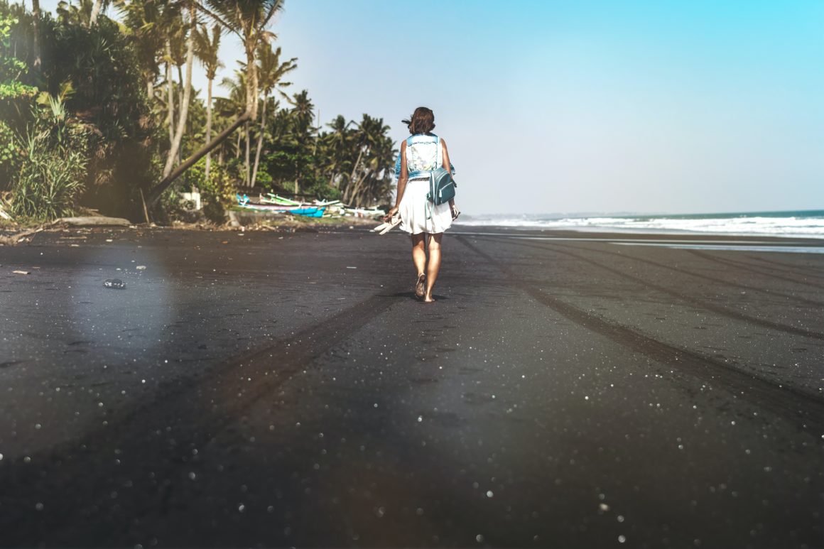 Person walking along the black sands of a beach in Bali