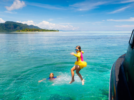 Kids jump into sea on a yacht vacation on exotic tropical island with crystal clear water, beach and swim fun.