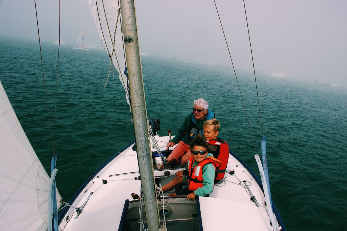 Two young boys and their grandfather on a sailboat wearing life vests.