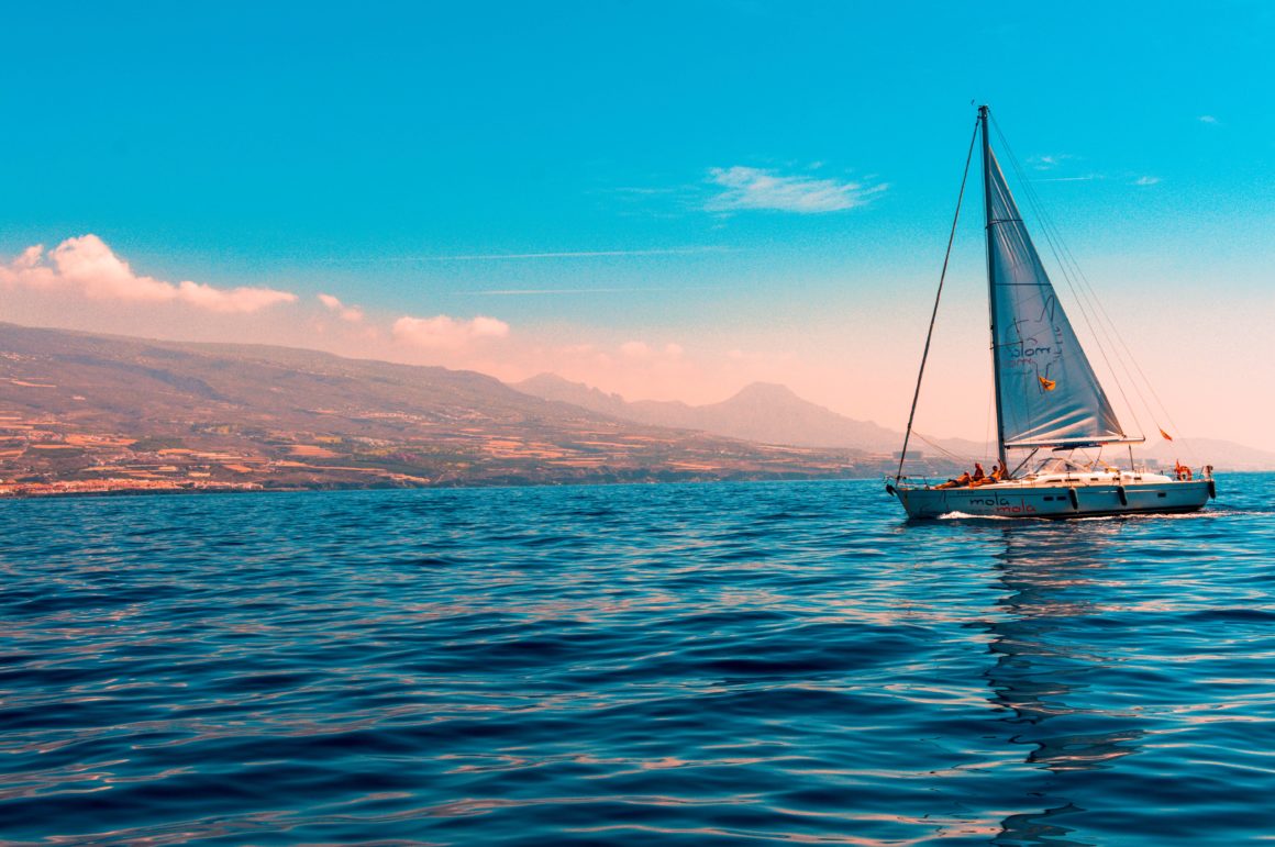 sail boat with blue sea and view of coast in the distance