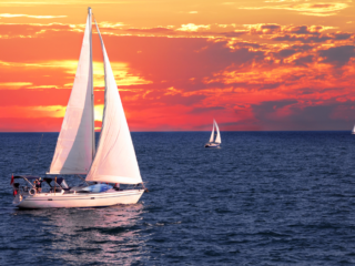 Cruising sailboat under full sail at sunset