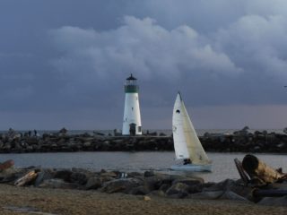 A sailboat sailing out of a bay with a lighthouse in the background