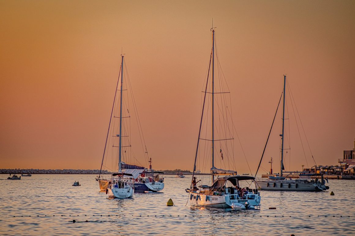 three sailboats in the water during sunset against an orange sky