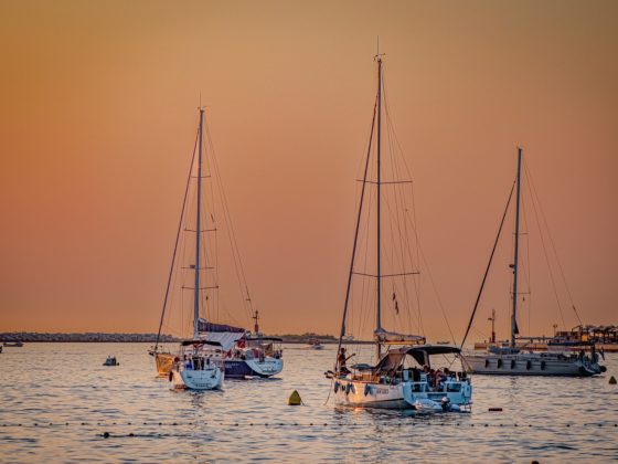 three sailboats in the water during sunset against an orange sky