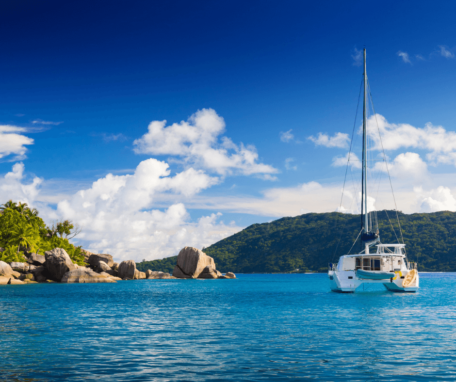 Catamaran in the sea at the Seychelles, rocky island to the left of the boat. Lush green covered mountain in the background