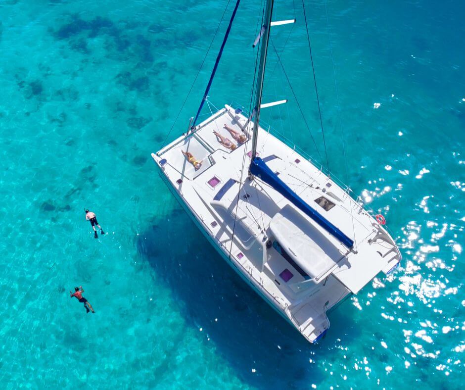 Image take from the sky of a big catamaran. People are snorkelling, swimming and sunbathing.