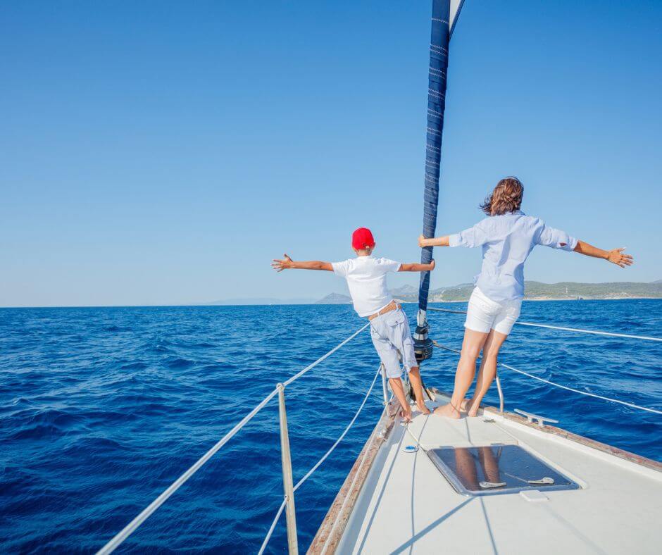 Image of a family on a sailboat, facing the blue sea with mountain in the background.