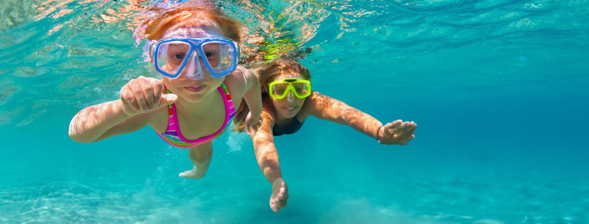 Image of two little girls snorkelling in the blue water.