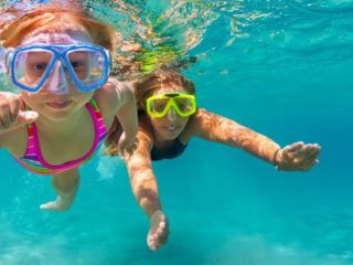 Image of two little girls snorkelling in the blue water.