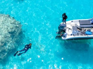 Aerial view of motorboat and three people in black wetsuits snorkeling in turquoise water