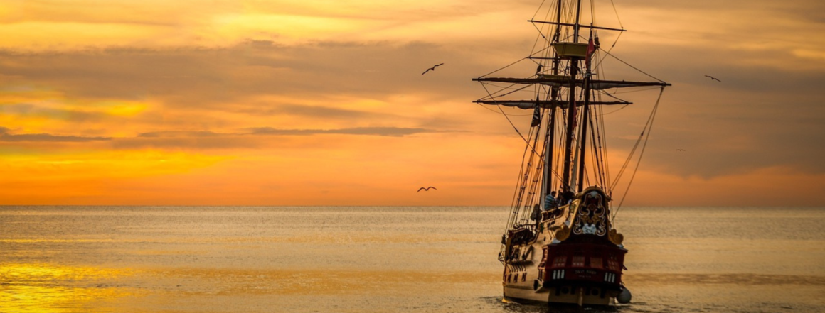 Old sail boat on the water, sailing into the sunset.